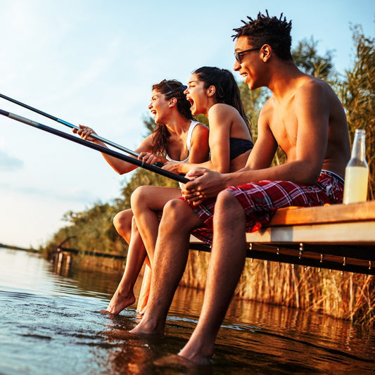 Group of friends sitting on pier by the lake and fishing.They joying in beautiful summer sunset.